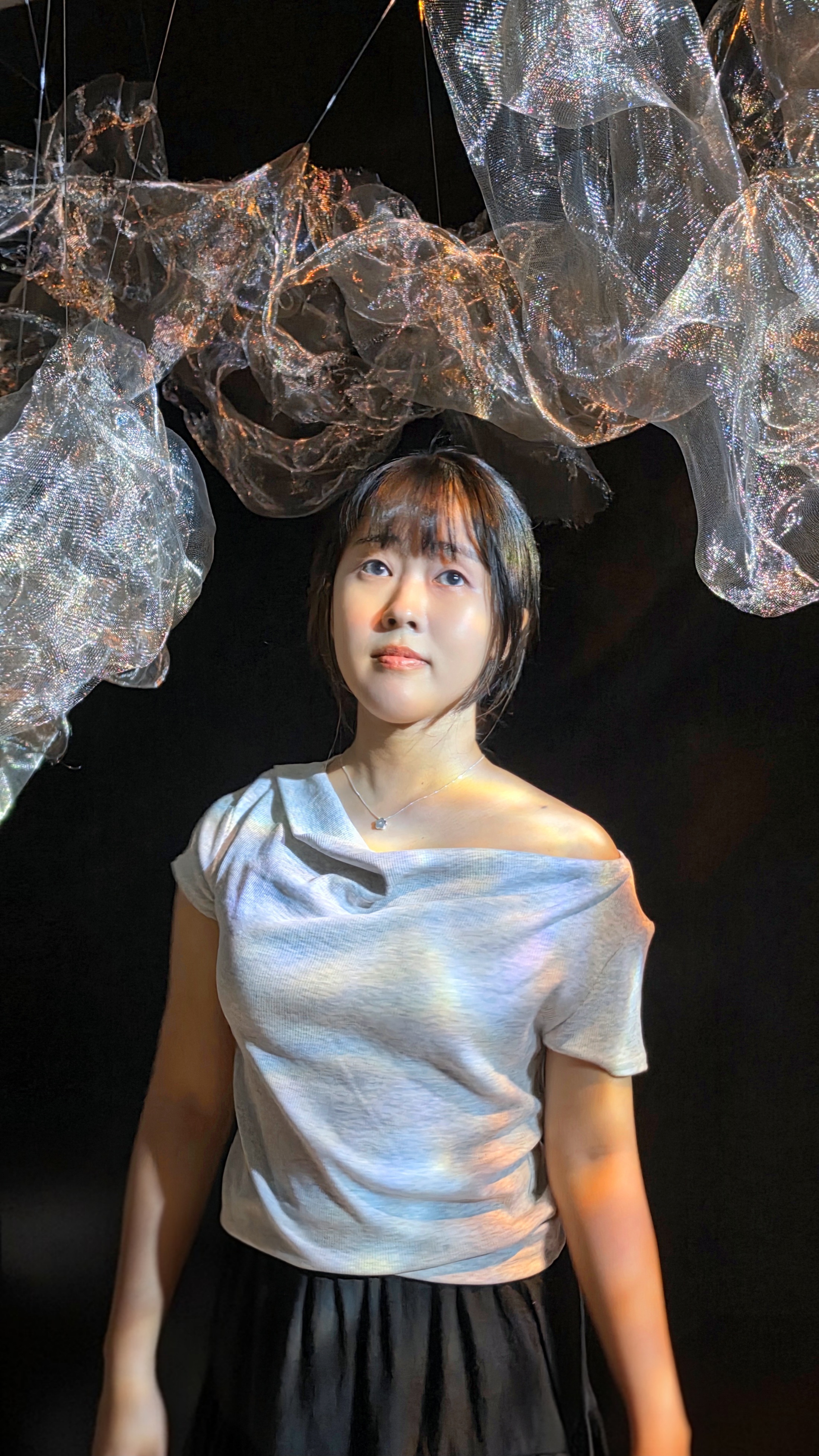 Kimberly Toh standing beneath an iridescent fabric installation